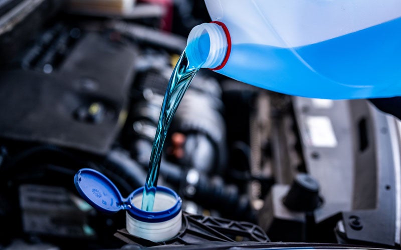 Blue engine coolant being poured into a vehicle's cooling system reservoir.